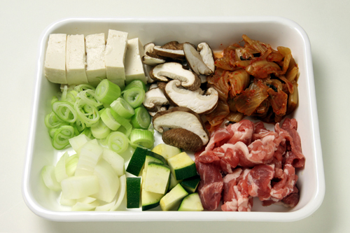 豚肉とキムチ、豆腐は一口大に切る。玉ねぎとズッキーニは1cm角、しいたけは薄切り、長ねぎは1/4ほど飾り用に小口切り、残りは5mm幅に切る。
