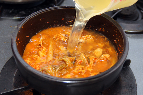 トゥッペギ又は土鍋に（2）を入れ、中火で炒める。肉に火が通ったらだし汁を加えて強火にし、煮立ったらチョングッチャンを溶かし入れ中火で3分ほど煮る。
