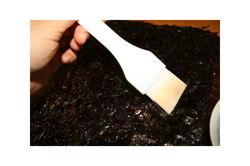 刷毛を使って、ごま油を海苔の片面に薄く均一に塗る。塩少々を指でつまみ、ごま油を塗った面の全体に振る。